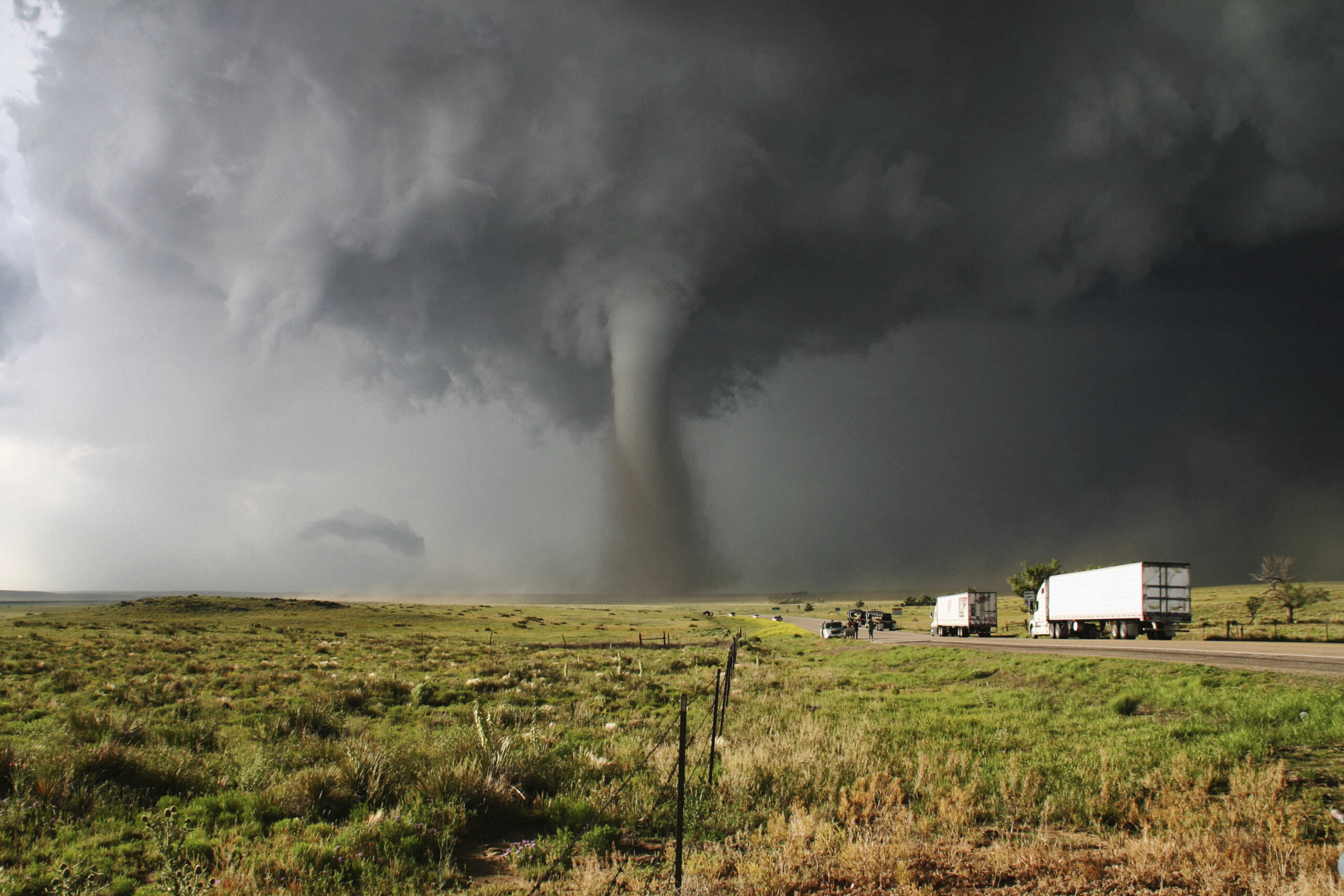 Vast tornado looming over a highway with trucks